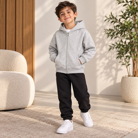 Boy in a light grey zip up hoodie and black joggers with white trainers, hands in pockets