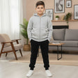 Boy in a light grey zip up hooded jacket with black joggers and white sneakers indoors