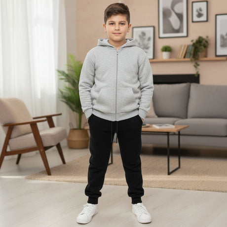 Boy in a light grey zip up hooded jacket with black joggers and white sneakers indoors