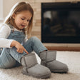 Girl pulling on grey kids winter boots by a fireplace