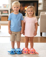 Boy in blue and girl in pink plush animal slippers standing on a rug by a fireplace
