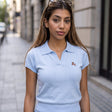 Light blue knit polo top with an open V collar and a small embroidered chest motif
