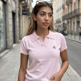 Pale pink knit polo top with an open neckline and tan embroidered motif