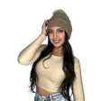 Woman pulling on a light brown cable knit beanie with a faux fur pom