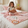 Girl on a bed with a pink character print blanket and plush bag
