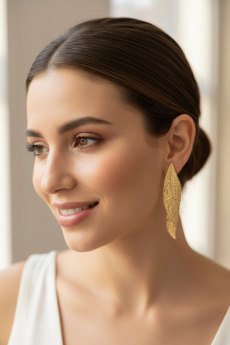 Woman wearing large gold leaf earrings with a neutral background