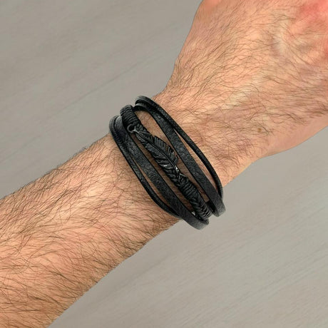Black leather wrap bracelet with a matte black feather charm on a wrist