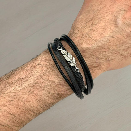 Black leather wrap bracelet with a silver feather charm worn on a wrist