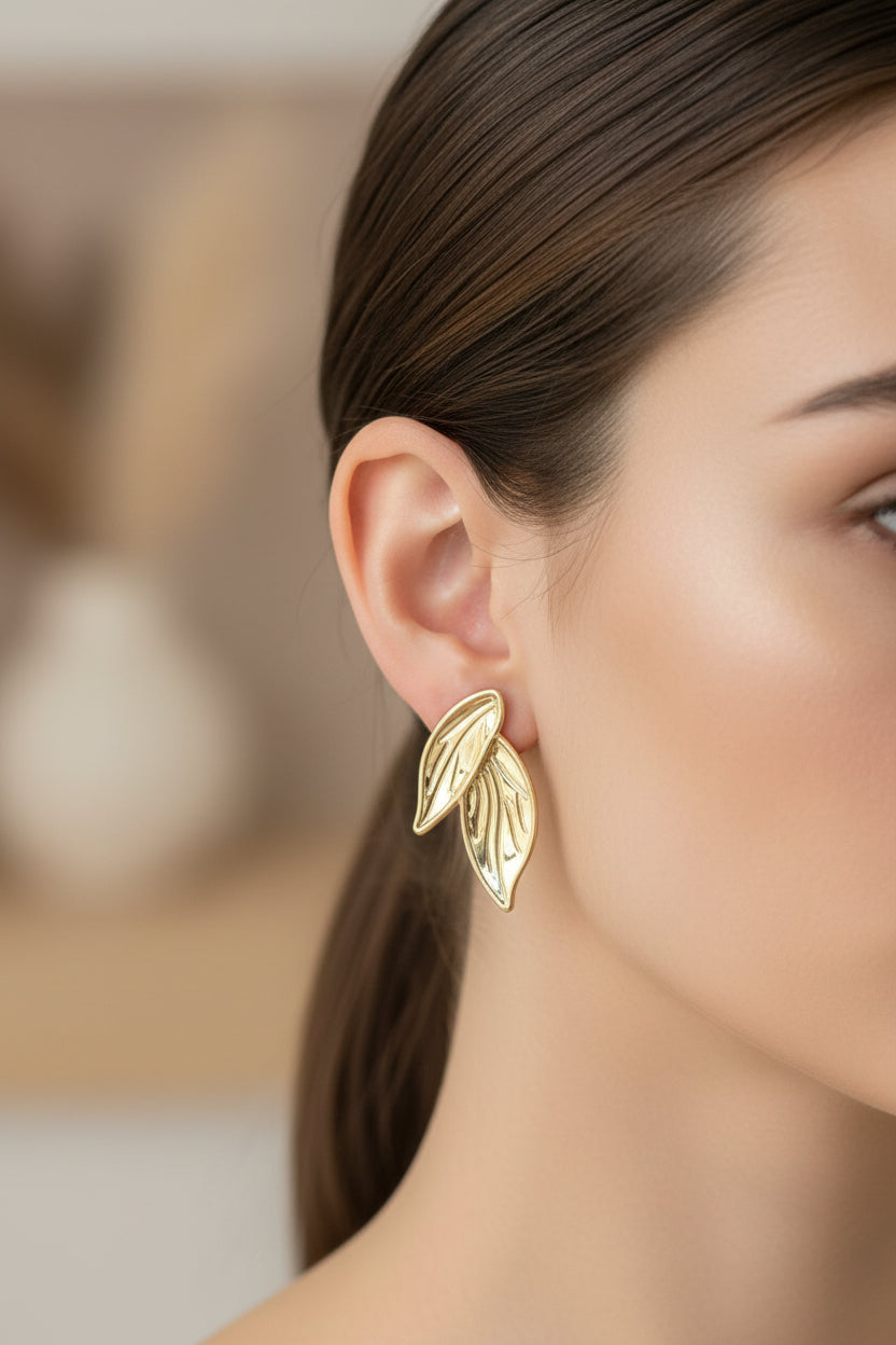 Gold leaf earrings worn by a woman with a blurred background