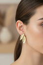 Gold leaf earrings worn by a woman with a blurred background