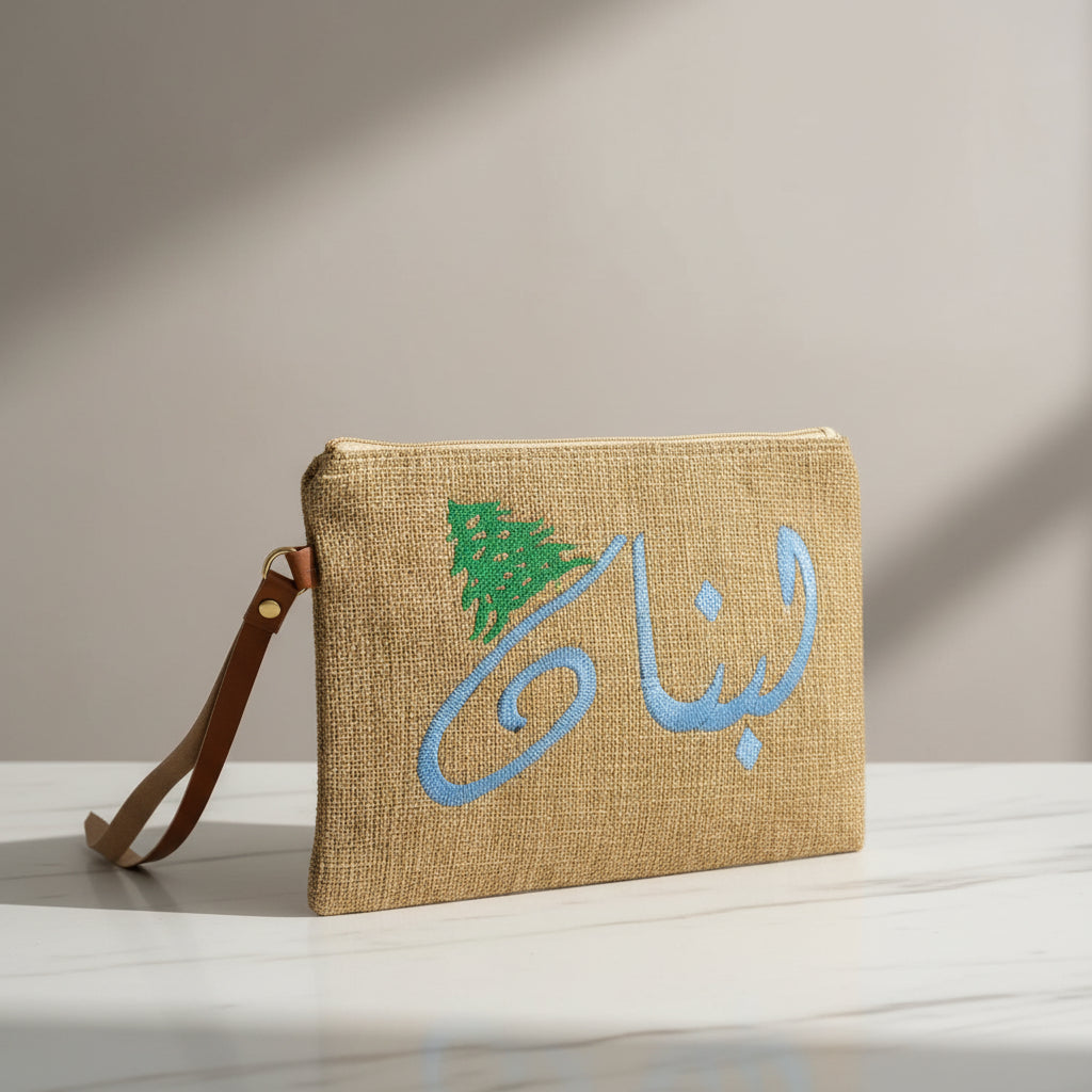 Jute zip pouch embroidered with Lebanon in pale blue Arabic script beside a green cedar