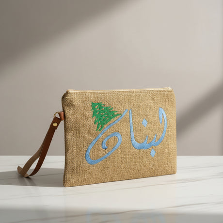 Jute zip pouch embroidered with Lebanon in pale blue Arabic script beside a green cedar