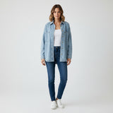Woman wearing a light blue denim jacket and dark blue jeans on a white background