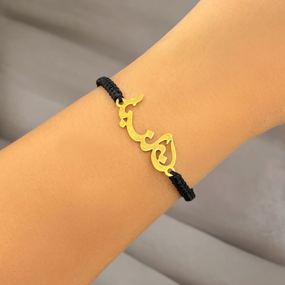 Gold Lebanon bracelet with black cord on a wrist against a neutral background