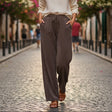 Woman walking on a cobblestone street wearing a white blouse and brown pants.