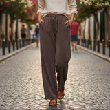 Woman walking on a cobblestone street wearing a white blouse and brown pants.