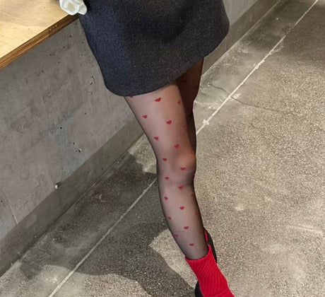 Person wearing black skirt and red heart-patterned tights with red socks on a concrete floor