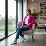 Woman in a fuchsia blazer sitting on a chair by a large window in a modern living room