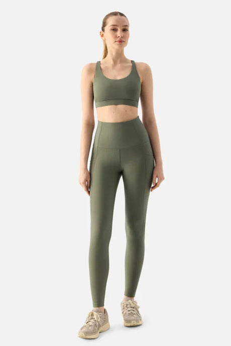 Woman wearing a green sports bra and leggings on a white background