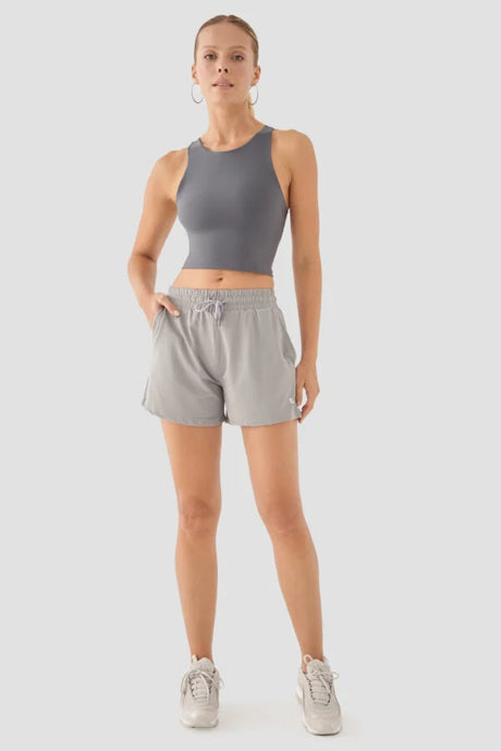 Woman wearing a grey tank top and shorts on a white background