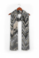 Grey scarf with gold patterns on a wooden hanger against a white background