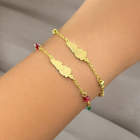 Gold bracelet with red, green, and gold beads and Lebanon's map on a wrist against a neutral background