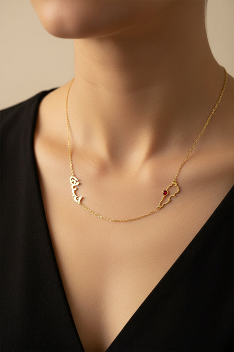 Gold necklace with arabic text and a lebanon map pendant on a model wearing a black top