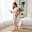 Woman in pink pajama set reading a book in a bedroom