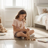 Young girl wearing a pink bear pj, playing with wooden blocks in a bright bedroom with teddy bears and books.