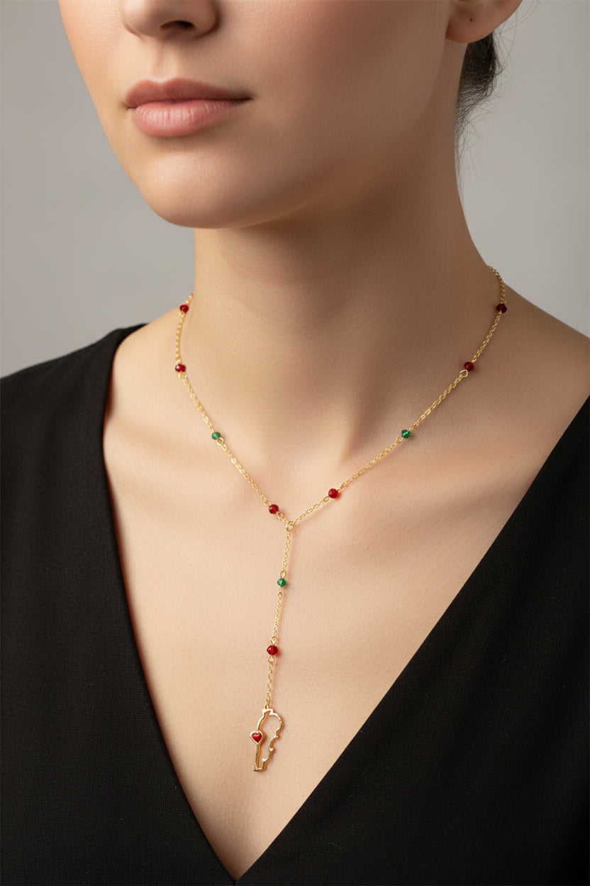 Gold necklace with red and green beads and a lebanon map pendant worn by a person against a neutral background