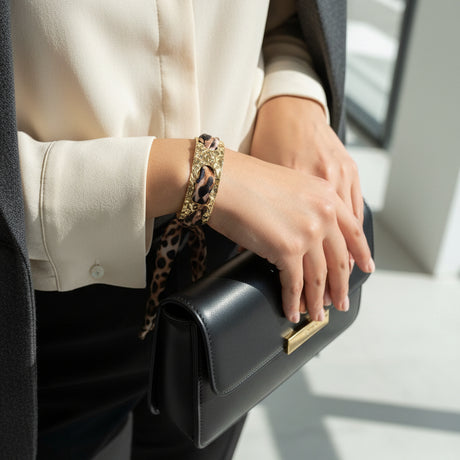 Gold bracelet with a leopard print pattern on a wrist, with a blurred indoor background