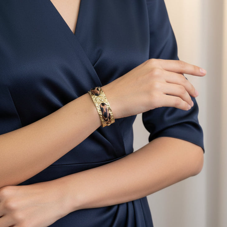 Person wearing a gold leopard silk cuff bracelet on a navy blue dress against a neutral background