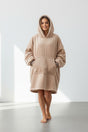 Person wearing a beige hooded garment in a minimalistic setting