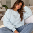 Woman in a light blue crew neck sweatshirt with minimalist Fiore lettering, worn with light jeans