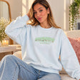 Woman in a light blue sweatshirt with mint green and silver sequin letters on the chest