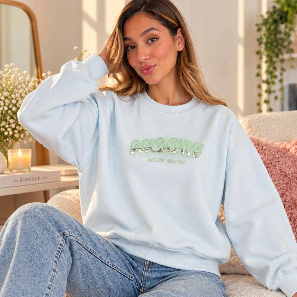 Woman in a light blue sweatshirt with mint green and silver sequin letters on the chest
