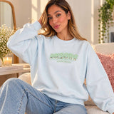 Woman in a light blue sweatshirt with mint green and silver sequin letters on the chest