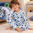 Boy in a light blue PJ set with a blue pixel game print, sitting on a fluffy rug by his bed