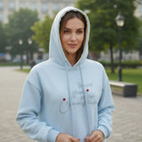 Woman wearing a light blue hoodie with a tonal script slogan and red dot accents
