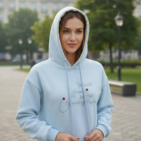 Woman wearing a light blue hoodie with a tonal script slogan and red dot accents