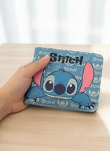 Hand holding a light blue bifold wallet with a peeking Stitch face and bold black lettering on top
