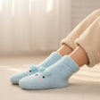 Light blue fuzzy socks with animal face design worn by a person on a neutral background