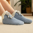 Light blue slipper socks with white fluffy tops worn indoors on a light-colored surface.