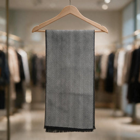 Light grey herringbone scarf with black fringed ends folded over a wooden hanger