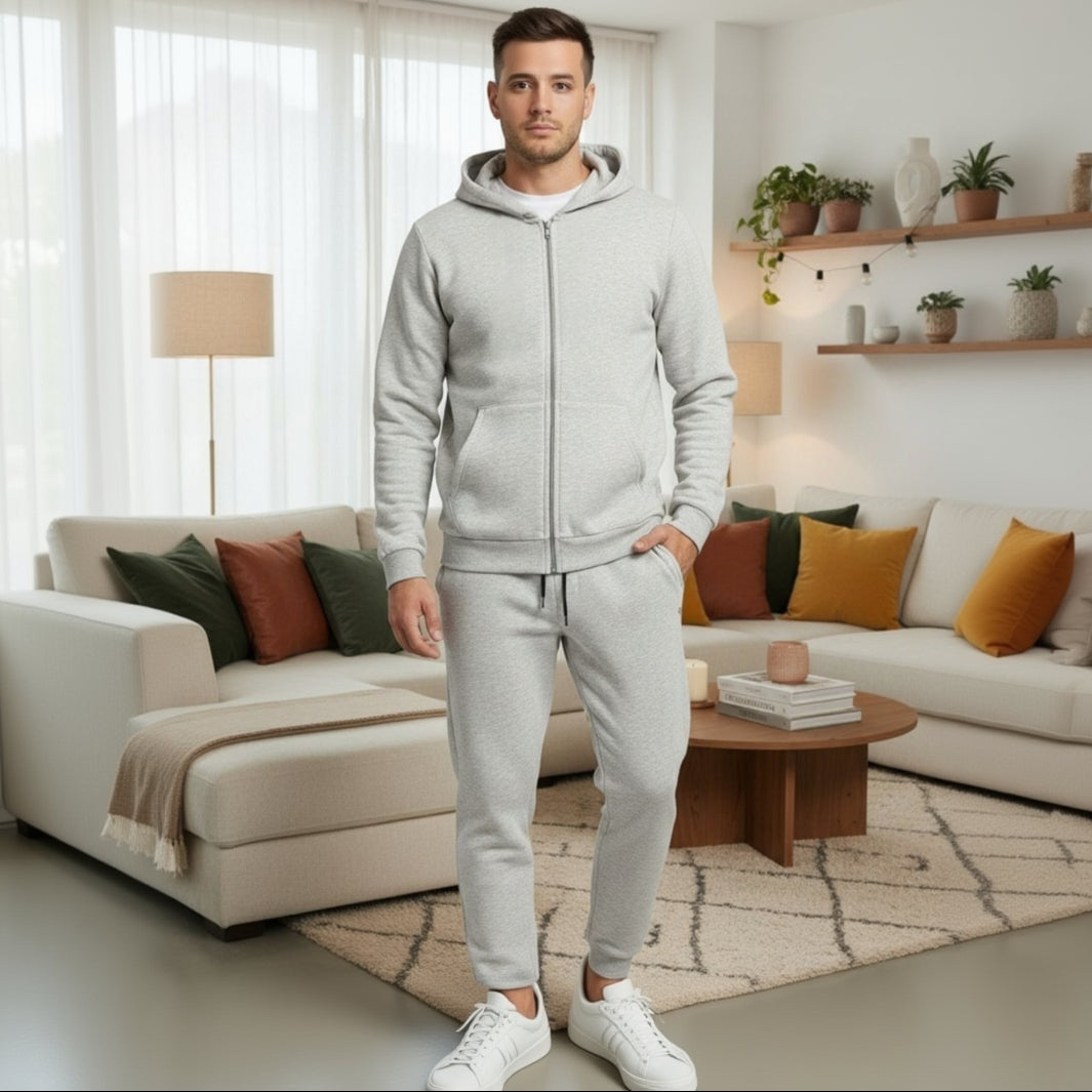 Man wearing a grey tracksuit standing in a living room with a beige sofa and decorative pillows