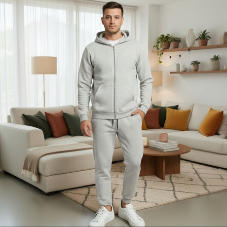 Man wearing a grey tracksuit standing in a living room with a beige sofa and decorative pillows