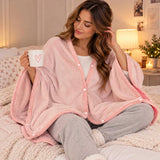 Woman sitting on a bed wrapped in a light pink fleece snap button blanket with pink trim, holding a mug