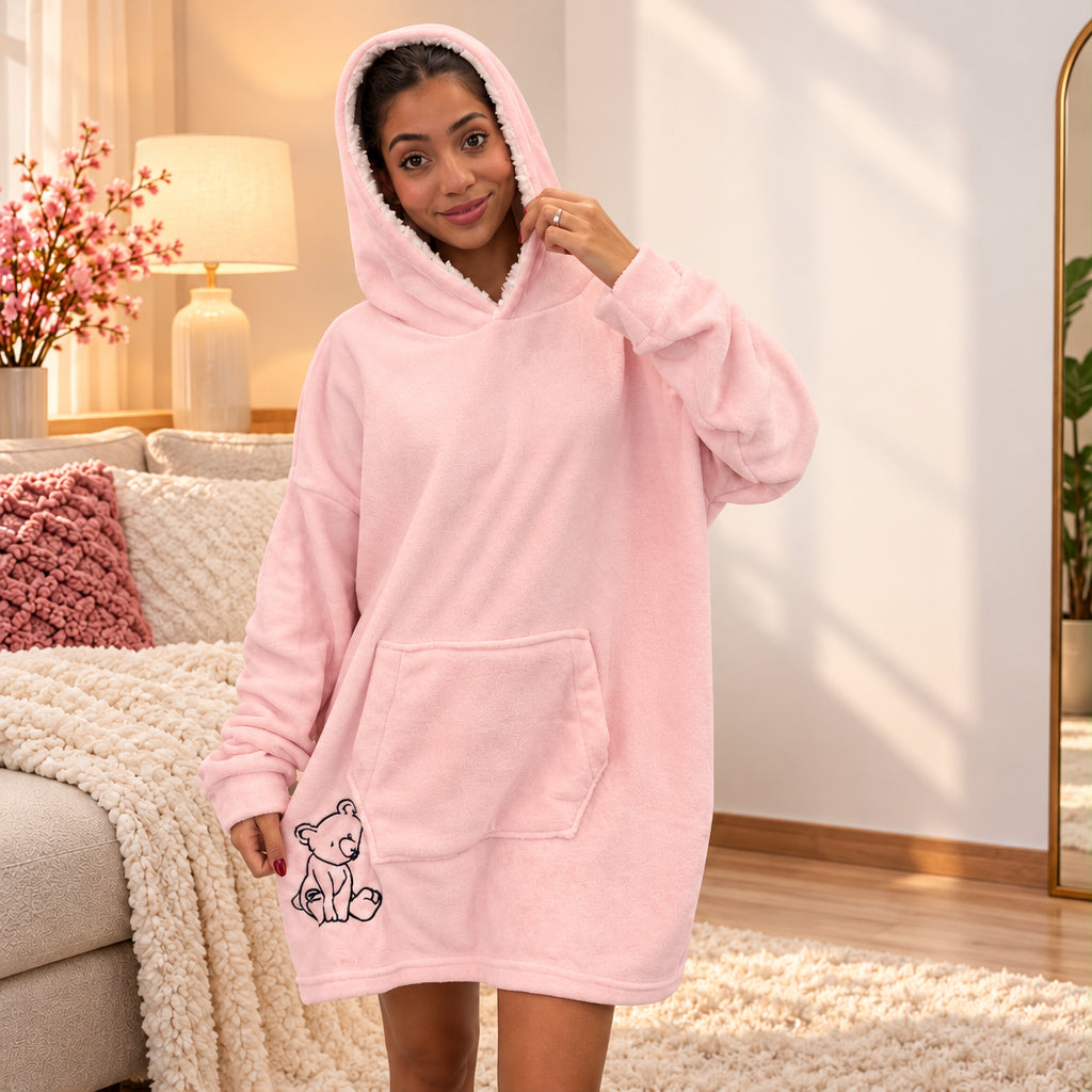 Woman in a pale pink fleece hooded blanket with the hood up and a bear outline near the hem