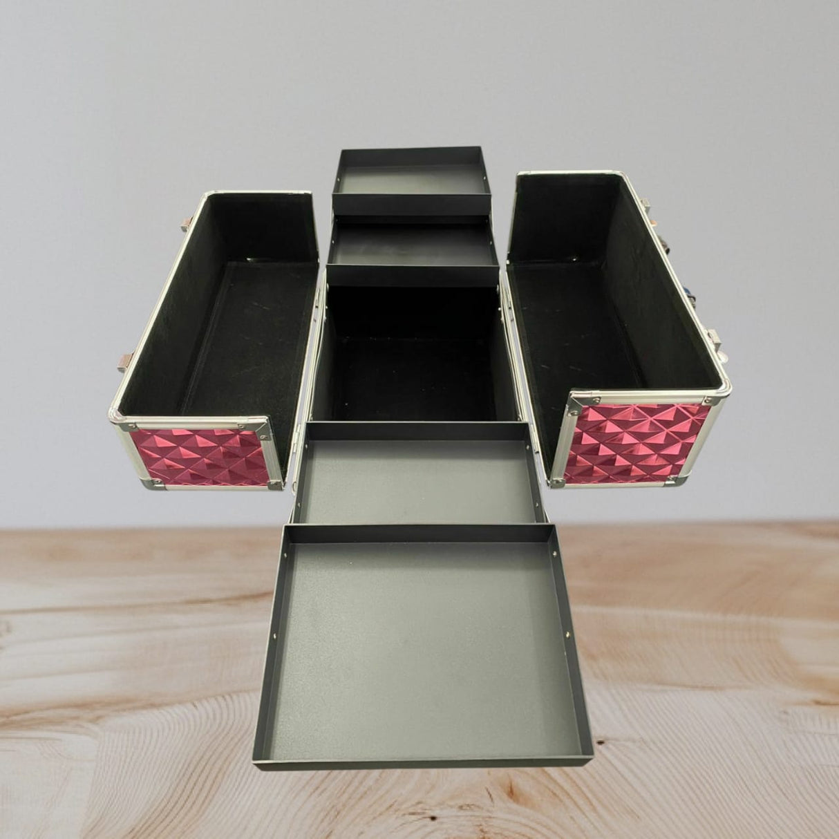 Pink aluminium vanity case with its trays swung out over a black lined base compartment