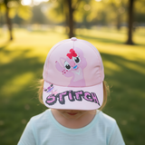 Girl outdoors in a pale pink cap featuring a pink cartoon character and bold peak lettering